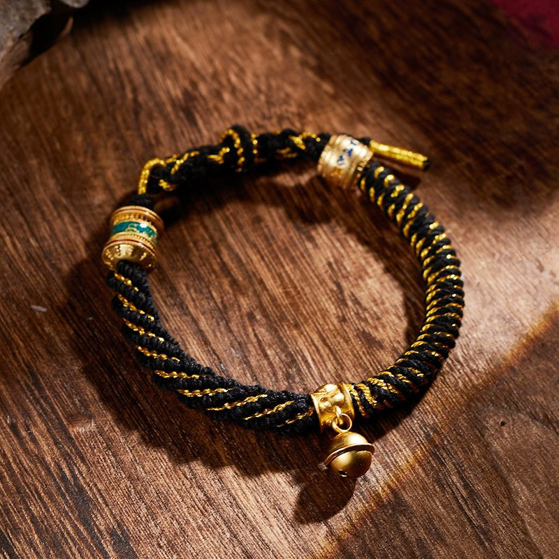 Black Tibetan knot bracelet with prayer wheel placed on driftwood