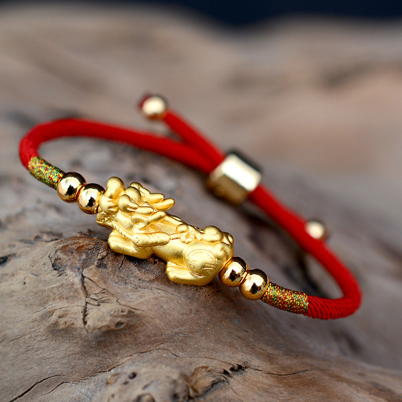 Gold Pixiu red string bracelet displayed on driftwood