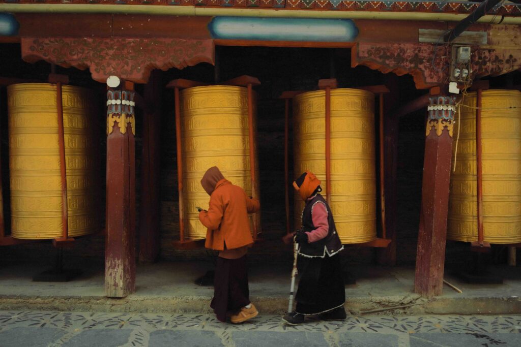 Two devoted practitioners recite prayers while spinning large Tibetan Buddhist prayer wheels at a monastery.